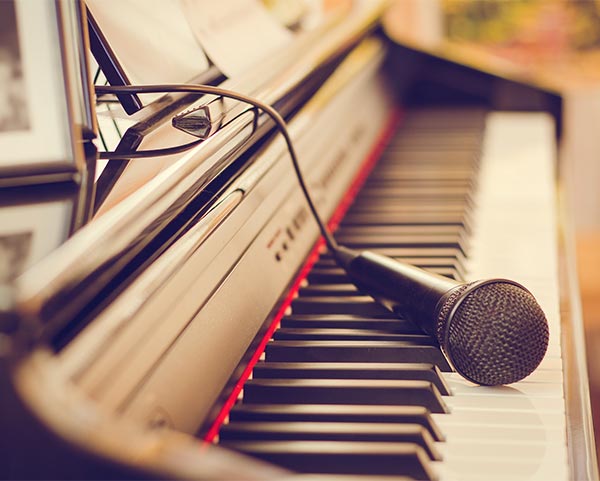 Gesangsunterricht und Klavierunterricht. Sie sehen das Foto eines Klaviers und eines Mikrofons.
